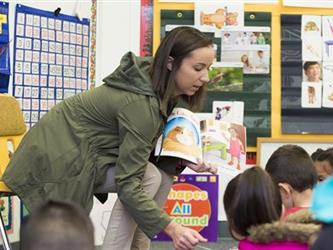 teacher reading book to three kids in classroom